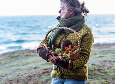 Portrait of Food Forager holding her haul of foraged food in her basket whilst wistfully looking out to sea. Food foraging has become popular in recent years as chefs have turned to foraged food to produce local and seasonal menu's. Photographed in Denmark.